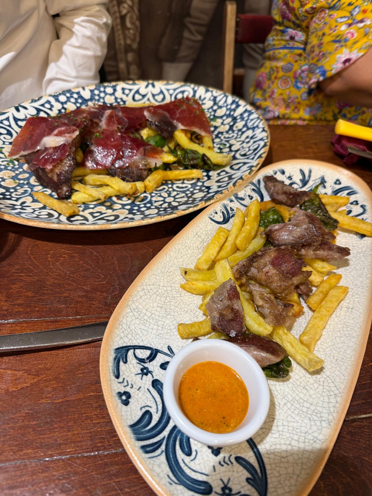 Pratos de carne com batatas fritas, pimentos e presunto numa mesa de restaurante