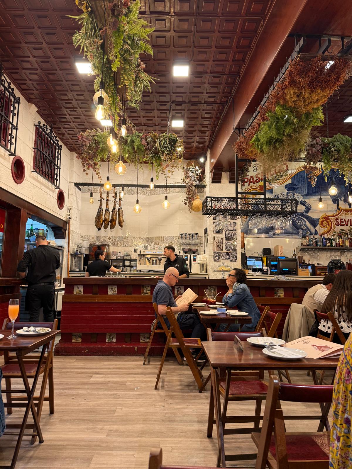 Sala de restaurante em Sevilha com balcão, mesas e decoração de plantas suspensas