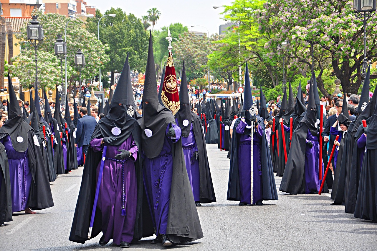 Participantes de uma procissão da Semana Santa, com túnicas roxas e capuzes negros, numa rua de Sevilha